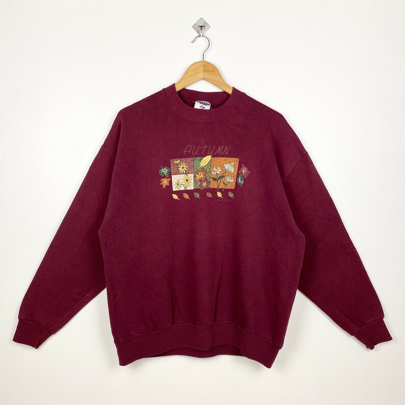 May include: A maroon sweatshirt with a graphic of autumn leaves and flowers. The text "AUTUMN" is printed on the front of the sweatshirt.