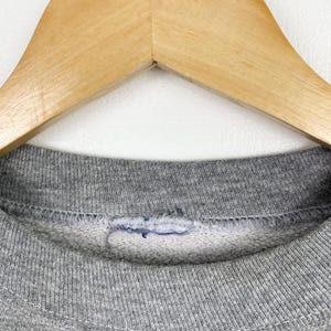 Puede incluir: Primer plano del cuello de una sudadera gris. El cuello es de canal&eacute; y tiene una sola puntada de hilo azul visible.
