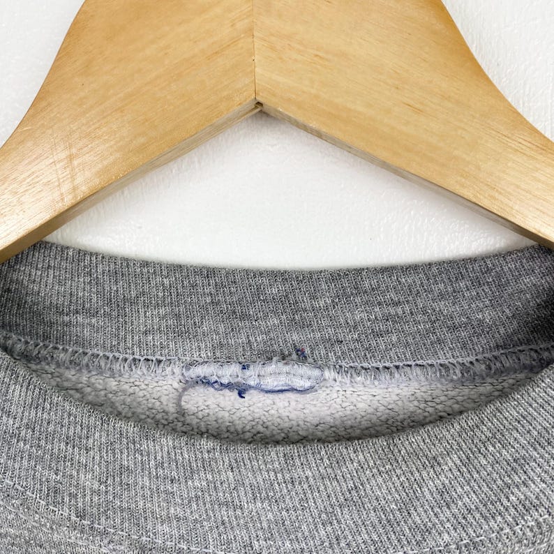 Puede incluir: Primer plano del cuello de una sudadera gris. El cuello es de canal&eacute; y tiene una sola puntada de hilo azul visible.