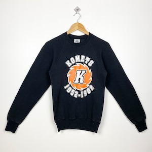May include: Black sweatshirt with a large orange and white graphic print that says "Komets K 1952-1992".