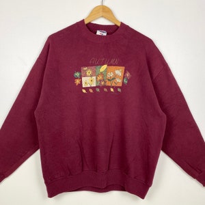 May include: A maroon sweatshirt with a graphic print of autumn leaves and flowers. The text "Autumn" is printed above the graphic.