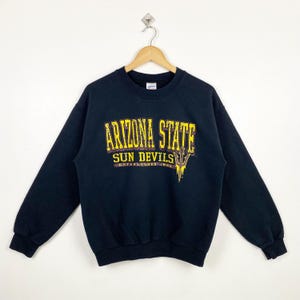 Puede incluir: Sudadera negra con un estampado gráfico amarillo y marrón que dice "Arizona State Sun Devils Established 1885".