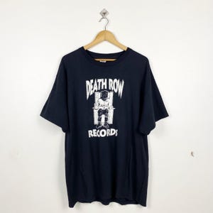Könnte beinhalten: Schwarzes T-Shirt mit einem weißen Grafikdruck einer Person, die auf einem Thron sitzt, mit dem Text "Death Row Records" darüber und darunter.