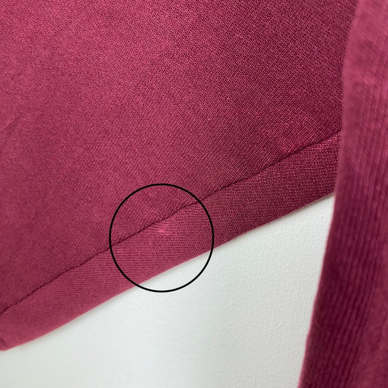May include: Close-up of a burgundy fabric with a seam running along the edge. The fabric is smooth and has a subtle sheen.