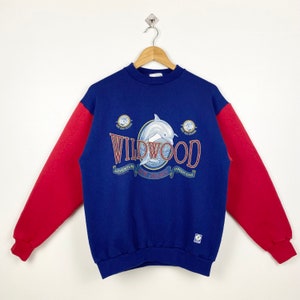 May include: Blue and red sweatshirt with a dolphin graphic and the text "WILDWOOD" with the words "ADVENTURE", "EXPEDITIONS", and "ON THE JERSEY SHORE" printed on a banner.