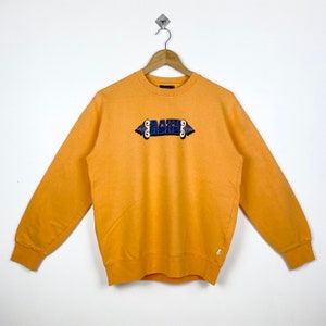 May include: A yellow sweatshirt with a blue and orange "Baker" logo on the front.