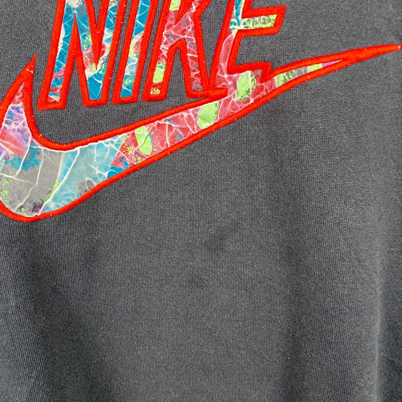 May include: A dark gray sweatshirt with a large, colorful Nike logo. The logo is made of a red outline with a multi-colored, abstract pattern inside.