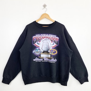 May include: Black sweatshirt with a graphic print of the 2001 World Series Champions Arizona Diamondbacks. The graphic features a baseball trophy with a baseball on top and the team's logo.
