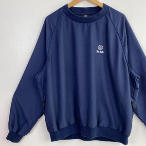 May include: Navy blue pullover jacket with a crew neck and long sleeves. Features a white logo on the chest and side pockets with zippers. The jacket is hanging on a wooden hanger against a white background.