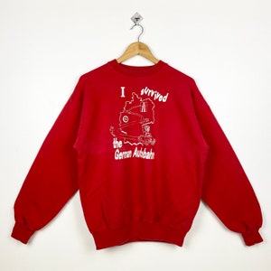 May include: Red sweatshirt with a white graphic print of a car driving on a highway in Germany. The text on the graphic says "I survived the German Autobahn".