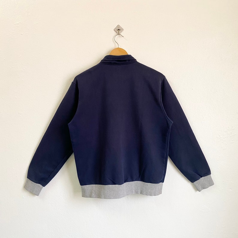 May include: A navy blue sweatshirt with a grey ribbed hem and cuffs. The sweatshirt has a zipper closure and a stand-up collar.