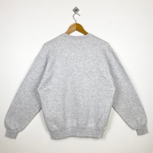 K&ouml;nnte beinhalten: Ein grauer Pullover mit Rundhalsausschnitt und langen &Auml;rmeln.