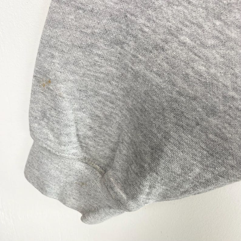 May include: Close-up of a gray sweatshirt sleeve. The fabric is a heathered gray with a slight texture. There are a few small brown stains on the sleeve. The cuff is ribbed and folded over.