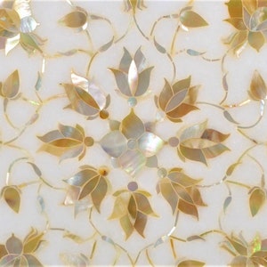 May include: A white marble surface with a floral design inlaid with mother-of-pearl and gold. The design features intricate floral patterns with delicate leaves and flowers.