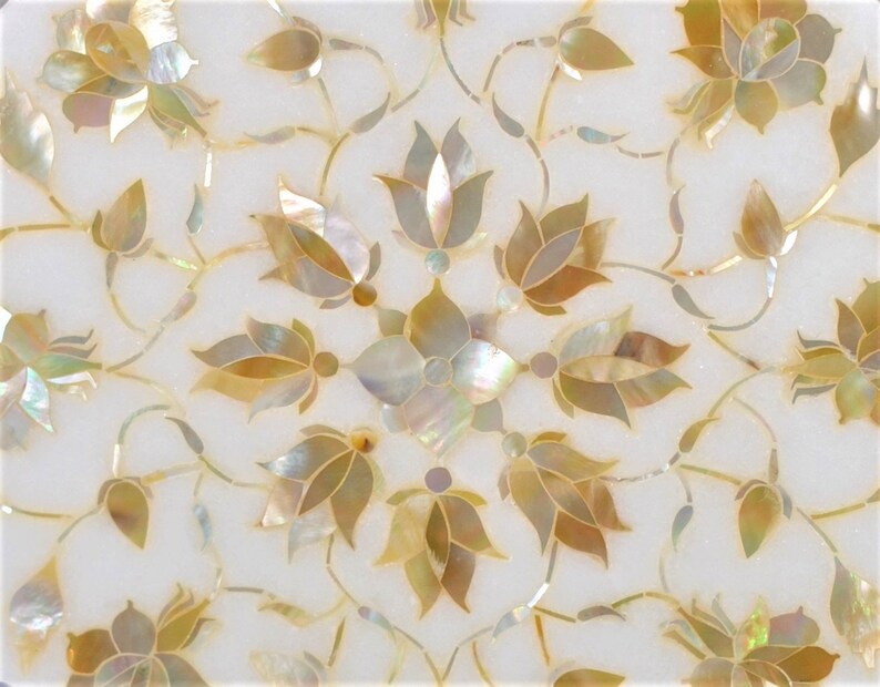 May include: A white marble surface with a floral design inlaid with mother-of-pearl and gold. The design features intricate floral patterns with delicate leaves and flowers.