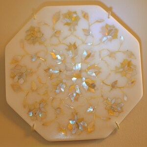 May include: A white octagonal tray with a floral design inlaid with iridescent mother-of-pearl. The tray has a delicate, intricate pattern of flowers and leaves.