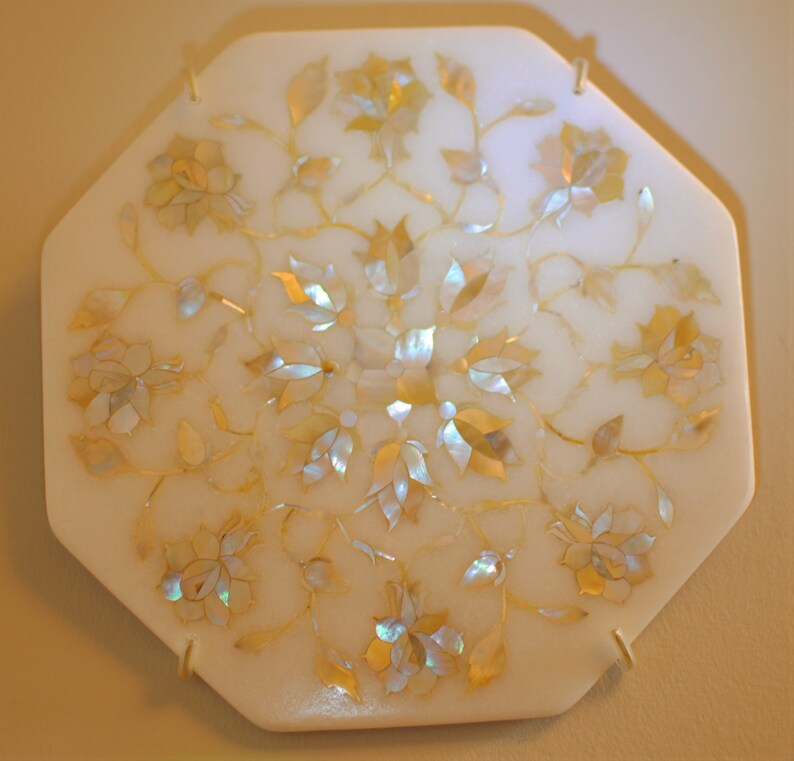 May include: A white octagonal tray with a floral design inlaid with iridescent mother-of-pearl. The tray has a delicate, intricate pattern of flowers and leaves.