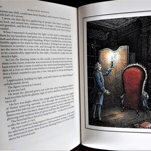 K&ouml;nnte beinhalten: Ein Mann in einem blauen Anzug und wei&szlig;em Hemd h&auml;lt eine brennende Kerze in einem dunklen Raum. Er steht vor einem gro&szlig;en, verzierten Holzspiegel. Ein roter Sessel befindet sich im Hintergrund.