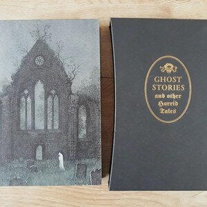 K&ouml;nnte beinhalten: Ein schwarzes Hardcover-Buch mit goldfarbenem R&uuml;cken und Titel. Der Titel lautet "Ghost Stories and other Horrid Tales". Das Coverbild ist eine Schwarzwei&szlig;illustration einer gotischen Kirche.