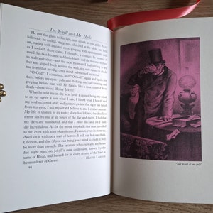 Pu&ograve; includere: Un primo piano di un libro aperto con un'illustrazione in bianco e nero di un uomo con un cappello a cilindro e un cappotto. L'uomo tiene un bicchiere e lo guarda. Il testo sulla pagina dice "Dr. Jekyll and Mr. Hyde" e "and drank at one gulp."