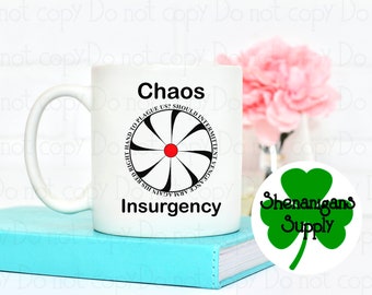 May include: White ceramic coffee mug with a black and white graphic design featuring a stylized wheel with a red centre. The text "Chaos" is above the wheel and "Insurgency" is below the wheel. The mug is sitting on a blue book. A green shamrock sticker with the text "Shenanigans Supply" is in the lower right corner of the image.