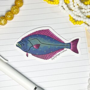 May include: A sticker depicting a flatfish illustration. The fish is blue with pink detailing on the fins and edges. The text "ShyShyShoppe Creations" is printed on the sticker.