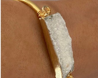 May include: A gold bangle bracelet with a white quartz crystal wrapped in gold wire.
