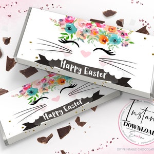 May include: Two white chocolate bar wrappers with a floral bunny face design. The wrappers feature a bunny face with a flower crown, eyelashes, and the words "Happy Easter" on a black banner. Chocolate pieces are scattered around.