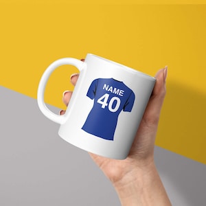 May include: White ceramic mug with a blue and white football jersey design. The jersey has the text "NAME" and the number "40" on the back.