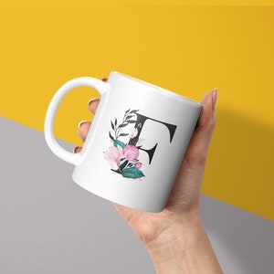 May include: White ceramic mug with a black letter "F" and pink and green floral design.