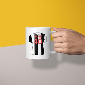May include: White ceramic mug with a black and white striped football jersey design. The jersey has the word "NAME" and the number "40" printed on it.
