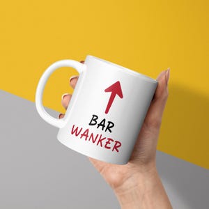 May include: White ceramic mug with a red arrow pointing upwards and the text "BAR WANKER" in black.