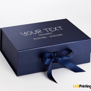 May include: A navy blue memory box with a matching ribbon closure. The box features the text "YOUR TEXT MEMORIES 25/02/1965 - 22/05/2022" in silver lettering. The box is a gift box.