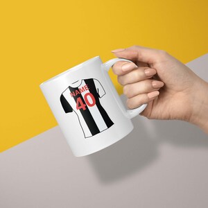 May include: White ceramic mug with a black and white football jersey design. The jersey has the word "NAME" and the number "40" printed on it.