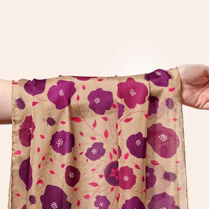 May include: A beige silk scarf with a floral pattern of pink and purple flowers. The scarf is tied around a person's wrist.