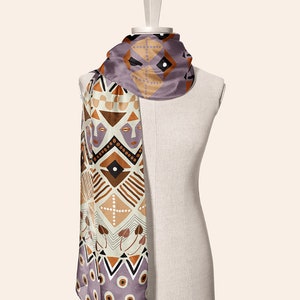 May include: A purple, brown, and white patterned silk scarf with geometric designs and stylized faces. The scarf is draped over a mannequin.