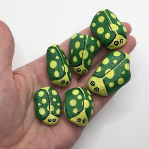 May include: Six hand-painted green and yellow ladybug rocks with black eyes. The rocks are painted to look like ladybugs with black eyes and yellow spots.