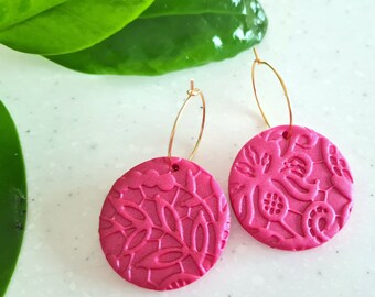 Op de afbeelding: Een paar roze creolen met een bloemenmotief. De oorbellen zijn gemaakt van polymer clay en hebben een gouden afwerking.