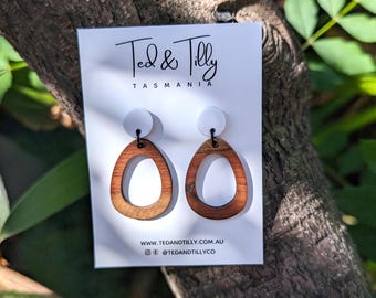 Op de afbeelding: Een paar houten oorbellen met een witte cirkel in het midden. De oorbellen zijn ovaalvormig met een uitsparing in het midden. De oorbellen bevinden zich op een witte kaart met de tekst "Ted & Tilly Tasmania" en website-informatie.