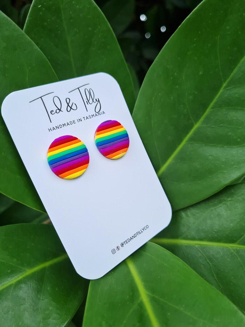 Op de afbeelding: Een paar regenboogkleurige oorbel studs op een witte kaart met de tekst "Ted & Tilly Handmade in Tasmania" en de social media handle "@tedandtillyco".