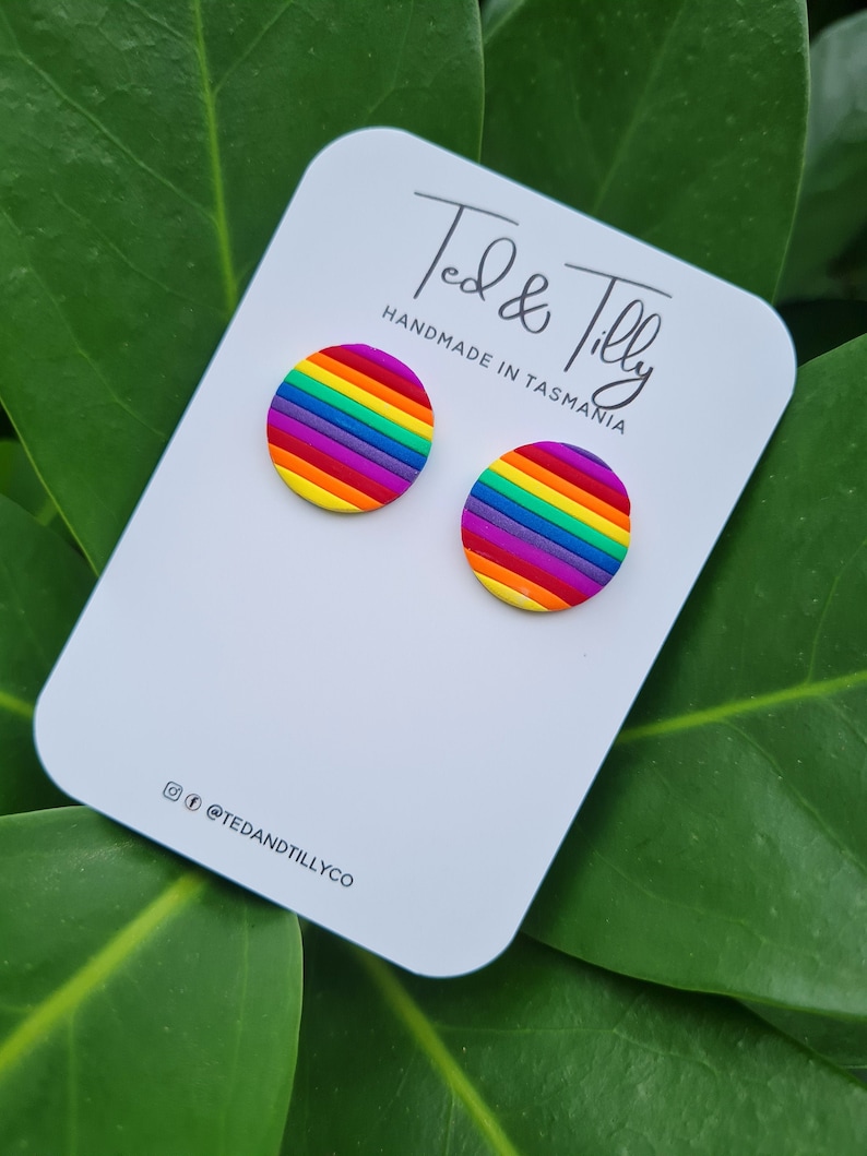 Op de afbeelding: Een paar regenboogkleurige gestreepte oorbel studs op een witte kaart met de tekst "Ted & Tilly Handmade in Tasmania" en de social media handle "@tedandtillyco".