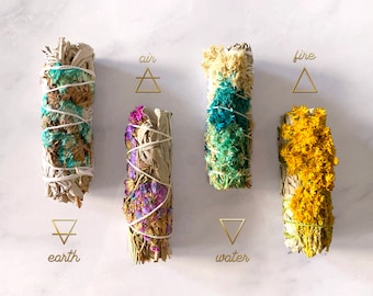May include: Five white sage smudge sticks with different coloured flowers and herbs. The sticks are labelled with the four elements: air, fire, earth, and water.