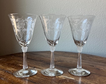 May include: Three clear glass wine glasses with etched floral designs on the bowl and a fluted stem.