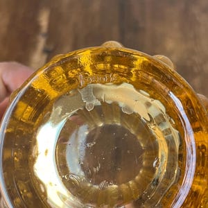 May include: The bottom of a clear amber glass vase with a textured surface. The vase has a round base and a wide opening. The text "131012" is visible on the bottom of the vase.