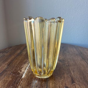 May include: A yellow glass vase with a fluted design. The vase has a scalloped rim and a rounded base.