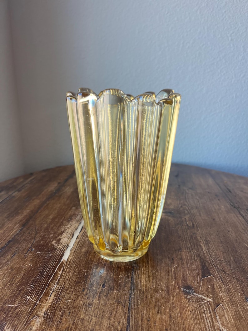 May include: A yellow glass vase with a fluted design. The vase has a scalloped rim and a rounded base.