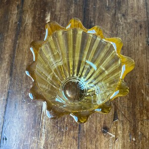 May include: A small, amber-colored glass bowl with a fluted design and a scalloped rim.