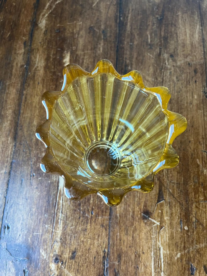 May include: A small, amber-colored glass bowl with a fluted design and a scalloped rim.