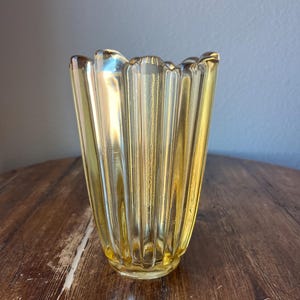 May include: A yellow glass vase with a fluted design. The vase has a wide mouth and a narrow base.