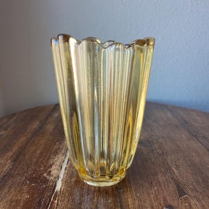 May include: A yellow glass vase with a fluted design. The vase has a wide mouth and a narrow base.